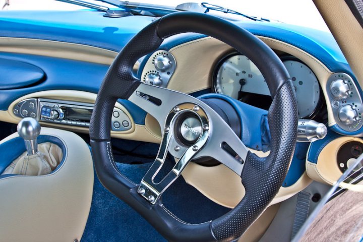 Pistonheads - The image showcases an ergonomic complex of the interior of a car with a focus on the steering wheel, gear shifter, pedals, and the side mirror. The steering wheel, a prominent feature, features a luxurious red-azure leather upholstery, installed by Bentley. From the gear shifter to the pedals, all elements are meticulously crafted with a Bentley badge, reflecting the brand's attention to detail and sophistication. The car's interior is a blend of comfort and functionality, designed to cater to drivers' every need while enhancing the driving experience.