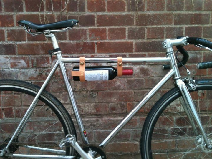 The "Show off your bike" thread! - Page 207 - Pedal Powered - PistonHeads - The image shows a close-up of a bicycle parked against a red brick wall. The bike is folded, with its frame resting on the brick wall. The wheels of the bicycle are distinct, one being black and the other silver. On the back of the bike is a wine bottle, which is securely fastened, suggesting that the owner may have biked to a destination for leisure or transportation of the wine.