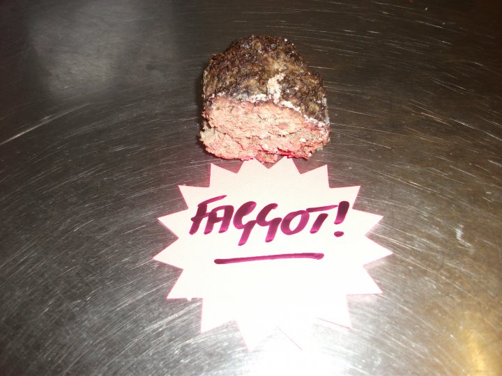 Pistonheads - The image presents a close-up view of food items and a sign on a metal table. The sign features two handwritten words, "FAGGOT!" and "FAGOT!!". The items include a slice of heart-shaped steak with a pink center, indicating it could be coated with pepper. Another piece of food is partially visible, likely a different cut of meat or precooked pasta.