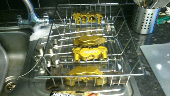 A close up of a box of doughnuts - Pistonheads - The image shows a kitchen sink with a dish rack on top of it. The dish rack is filled with various kitchen utensils, including silverware, measuring cups, and a knife. There are three yellow-shelled items in the dish rack; two appear to be tweezers, and one resembles a watering gun.