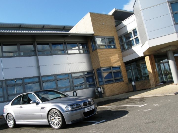 Local photo locations - Page 1 - East Anglia - PistonHeads - The image showcases a modern architecture office building, characterized by a curved entrance and multiple windows. A silver BMW car is parked in the foreground, creating a contrast with the building's modern design. Above the building, a blue sky is visible with some clouds scattered across it. The overall scene suggests a sunny day in a city or urban environment. The windows on the building appear to be reflecting patches of the sky, adding an interesting visual element to the scene.