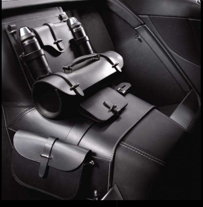 Interesting Custom Luggage Option - Page 1 - Aston Martin - PistonHeads - The image displays the interior of a luxury vehicle, specifically focusing on the console of the car. There is a collection of items neatly arranged on the center console. A black leather case is open, revealing a creme-colored book and what appears to be a silvertone mechanical device or switch with elegant black handles. Resting on top of the open case is a toolkit with a smooth, dark surface and embossed silver-colored clasps. This setup suggests a serious attention to detail and a luxurious taste in accessories for the car.