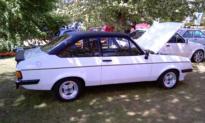 Cars On The Green - Photo Thread - Page 1 - East Anglia - PistonHeads - The image captures a classic white car showcasing a white car hood that is up. The car, which appears to be a Fiat, is parked on a grassy field under sunny skies. The setting implies an outdoor auto show or exhibition. The viewers will find the classic design, white car hood, sunroof, and black wire wheels quite charming. The car is surrounded by other vehicles and people, suggesting it's part of a larger display or event.