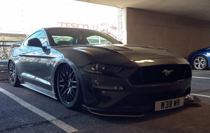 Spotted In South Wales (Vol 3) - Page 322 - South Wales - PistonHeads UK - The image showcases a black Ford Mustang GT, which is parked in a parking lot. The car is positioned facing the camera, with its wheels turned slightly towards us. It's parked next to a white line that marks the boundary of the parking space. The Mustang features a distinctive body kit and custom paint job, giving it a unique and sporty appearance. The license plate of the vehicle is clearly visible. There are also other cars parked in the vicinity, but they are not as prominently featured.