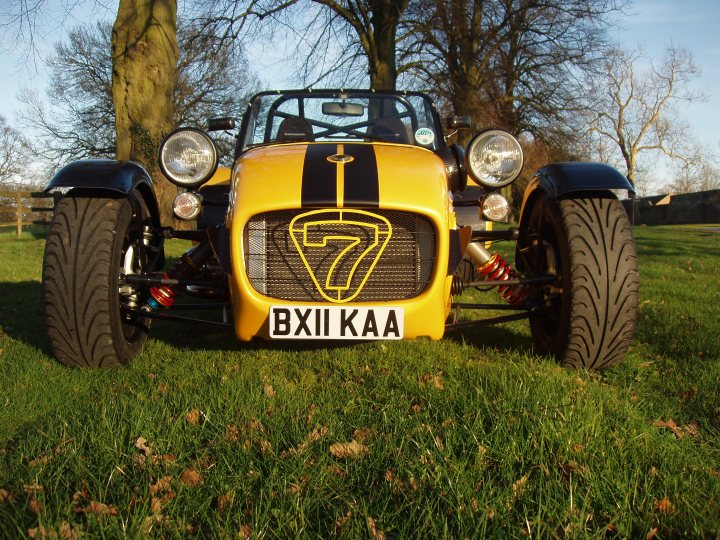 Pistonheads Chassis Duratec Imperial - The image is a photograph of an eye-catching "7" rally car, which is yellow with black accents, parked in a grassy field. The car's distinctive feature is a grille adorned with the number "7" and the letters "BXXIIKAAA," with a lion emblem located at the center. The vehicle is equipped with large front and rear bumpers, as well as thick, off-road tires that are partially hidden by the grass. The scene suggests an outdoor setting, possibly on a racing or off-roading track, and the time appears to be daytime with plenty of natural light illuminating the scene.