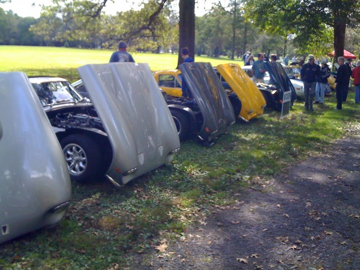 Woodwork Pistonheads - The image showcases an outdoor auto show, with a cluster of antique and classic cars on display. Some of the cars are open, revealing their interiors, while others are closed. The cars are parked on a grassy area under a tree, creating a serene and picturesque setting for the event. A group of people, likely attendees of the show, are scattered around the area, observing and admiring the classic vehicles.