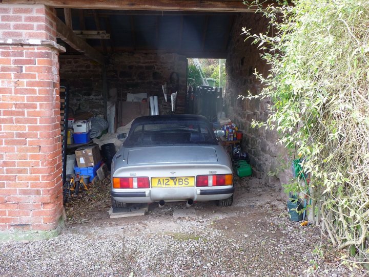 How do you keep yours? - Page 3 - S Series - PistonHeads - The image shows a grey car parked inside a garage with a brick wall. The garage appears to be old and constructed of brick, giving the scene a rustic feel. A few greenery can be seen near the car, suggesting that the garage opening is accreptated with grass and bushes. Next to the car, there is a blue bucket and what appears to be a spare tire.