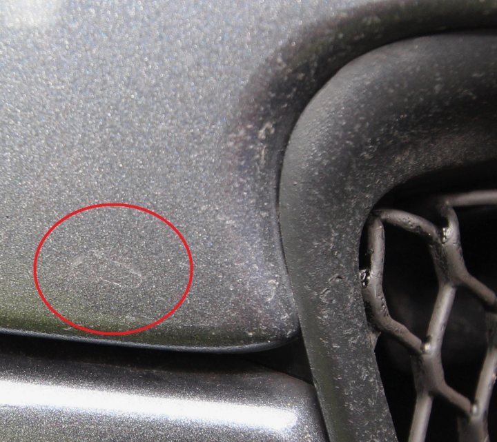 A close up of a car parked on a street - Pistonheads - The image is a close-up of a car's component, possibly a piece of the vehicle's frame or engine shrouding. The focus is on a small, indistinct speck or marking located centrally in the frame, inside a red-bordered circle. The component appears metallic with a matte finish, and there is a pattern that resembles a fine mesh or a crosshatch design. This could be part of a mechanical system, but due to the close-up and the indistinct nature of the marking, it is challenging to identify the specific component or the purpose of the marking.