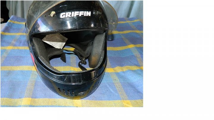 A close up of a person on a motorcycle - Pistonheads - The image displays a view of the side of a black helmet on a fabric surface with a plaid pattern. The helmet is a motorcycle helmet, as indicated by the label "GRIFFIN" on the side. There is a black visor that is pulled up, revealing the inside which appears to be damp or wet. The helmet has vent slits at the bottom and is secured to the chin with a black strap. The fabric underneath the helmet has shades of blue and yellow. The photo seems to be taken from a slightly left angle, showing the side of the helmet and part of the back.