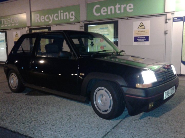 NEW RENAULT 5 GT TURBO OWNER :D - Page 1 - French Bred - PistonHeads - This image captures a small black Volkswagen parked in front of a store. The car is positioned on a gravel driveway, with the front facing the camera. Its color contrasts with the surrounding environment. Above the car, a green sign reading "Recycling" and "Centre" suggests that this area might be near a recycling center. The lighting in the photo hints at being taken in the evening or early morning.