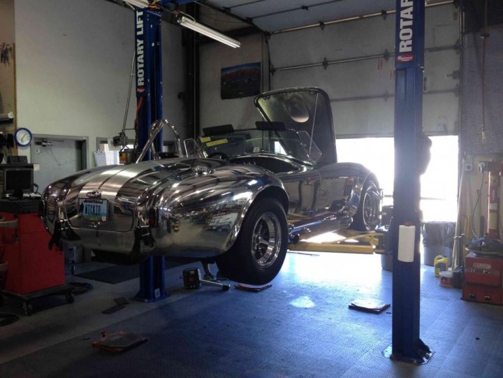 A car is parked in front of a building - Pistonheads - The image shows a garage scene where a vintage car with an unusual design is hoisted on a hydraulic lift. The car has a polished, silver finish and features unique design elements. The garage is equipped with various tools and materials, indicating a space well-used for vehicle maintenance and repair. A person can be seen in the background, likely involved in the mechanics of the garage.