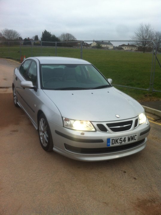 Got it - 9-3 Aero... - Page 1 - Saab - PistonHeads - The image shows a silver-colored, four-door sedan parked on a concrete surface, likely a parking area. The car is in the foreground of the photo with its front facing towards the viewer. Behind the car, there is a chain-link fence, possibly indicating a security area or a controlled parking zone. The fence encloses a grassy area that appears to be a field or a part of a larger outdoor space. The sky is overcast, suggesting either an early morning or late afternoon setting. The image seems to be an everyday scene rather than one of extraordinary nature.