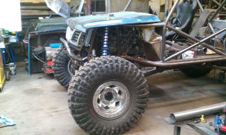 Pics of your offroaders... - Page 54 - Off Road - PistonHeads - The image depicts a scene in a garage where a disassembledvehicle, possibly a quad buggy or dune buggy, is being worked on. The central focus of the image is a large black tire with ridges, suggesting it's designed for off-road capabilities. The vehicle appears to have a robust construction, highlighted by its sturdy roll cage structure, built for safety or connection for a motor. The garage environment suggests mechanical work is being performed; tools and parts are scattered around, with at least one other vehicle visible in the background.