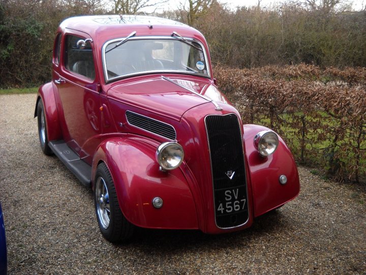 A red truck is parked in a field - Pistonheads - The image showcases a vibrant red vintage car parked on a gravel driveway. The car exudes a classic charm, equipped with black wire wheels, and is adorned with white license plates and a silver nameplate. The car's detailed hood ornament and grill size reflect its antique design, adding to its vintage appeal. The surrounding environment includes a neatly trimmed hedge and a few trees in the background, contributing to a serene ambiance.