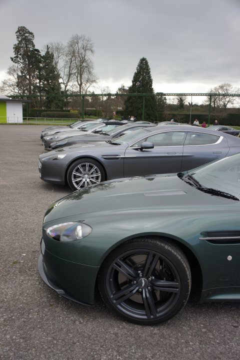 Beaulieu Run - Page 1 - Aston Martin - PistonHeads - This image shows a row of parked luxury cars on a clear day. The cars are fleet vehicles, likely part of a luxury car rental or leasing business, as indicated by the similar color scheme and makes. The vehicles are parked side by side, creating an orderly line that extends towards the horizon. The cars' sleek designs, along with the absence of any visible branding, suggest they are high-end models. The environment is mostly greenery and a clear blue sky, adding to the scenic ambiance of the setting.