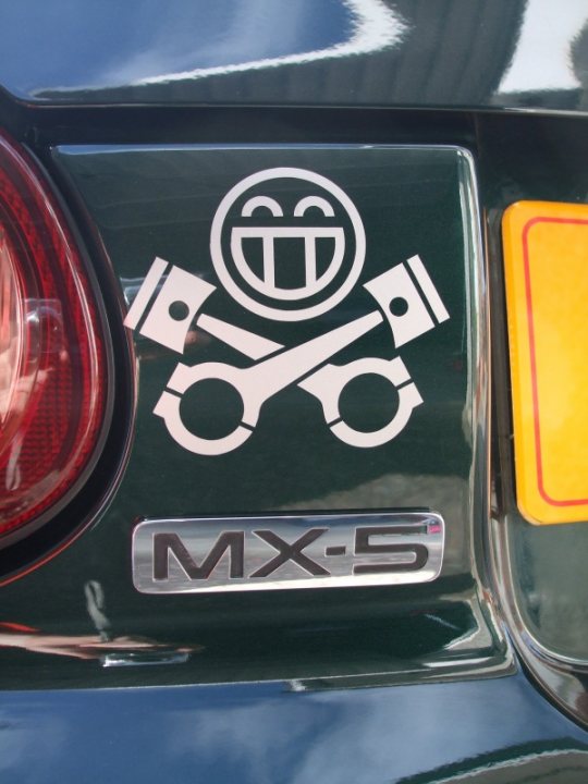 Weight Feather Cruiser Pistonheads Bruiser - The image is a close-up photograph of a section of a vehicle, specifically showing the tail light and a tailgate emblem. The tail light is visible from within to the outside, and the emblem is metallic, featuring a logo that includes a smiling face, a wrench, and a screwdriver crossed above a logo that reads "MK-5." The name "Tailgate" is also present, indicating the brand or model of the car.