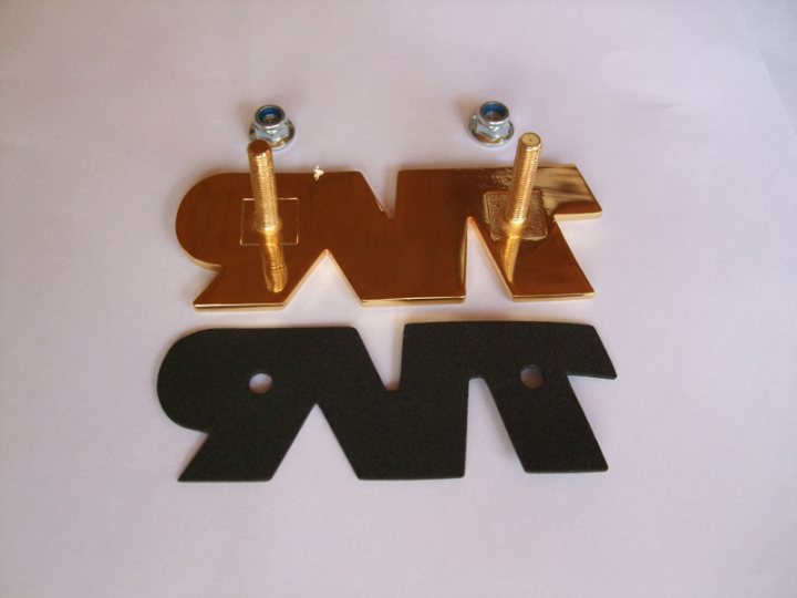 The 2011 TVR Union Jack Badge Thread! - Page 1 - General TVR Stuff & Gossip - PistonHeads - This image showcases two identical cutouts, likely made of endearing filigree, resting on a white background. The elongated black shapes bear resemb|ance to the word "swt:" containing "m," "w," and "t," accompanied by two screws on top for attaching the cutouts to a surface. The text and the cutouts appear to be paired together to form a decorative or functional piece. The overall arrangement suggests a minimalist and modern design aesthetic.