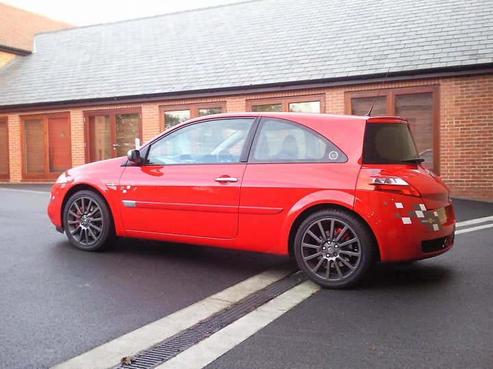 South West PH Car Photos inside... - Page 1 - South West - PistonHeads - The image features a red compact car parked on a black paved surface. The car has a distinctive two-door hatchback design, characteristic of many small, sporty vehicles. One of the most striking features is the black rims that completely cover the wheels, offering a bold contrast against the car's fiery hue. The vehicle is captured during the daytime, with clear visibility of its surrounding environment. The background showcases a brick building, suggesting an urban or suburban setting.