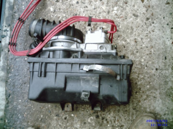 Any ideas what this is off? - Page 1 - General Gassing - PistonHeads - This is a close-up image of a mechanical part, specifically the starter motor for a vehicle. The starter, with its red cables running into it, is part of the vehicle's electrical system. The motor is disc-shaped and has been removed or placed out of context as it is not installed on an engine. The cables are thick, and the metal components are mostly gray in color. The background is a rough concrete surface, making it a practical image rather than an artistic one.