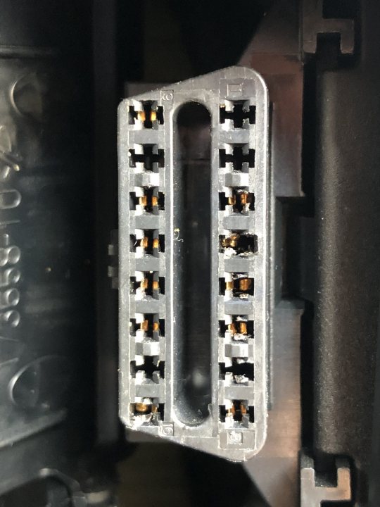 F30 OBD port issues - Page 1 - BMW General - PistonHeads UK - The image shows a close-up view of an electronic device component, specifically what appears to be a small circuit board with multiple electronic components attached. The board is densely packed with several gold-colored contacts on one side and numerous holes or connectors on the other. There's a visible yellow substance near some of these connectors, possibly indicating a manufacturing process in progress or a test being performed. The component is partially obscured by its surrounding elements, making it difficult to discern the exact function of this part within the larger device it belongs to.