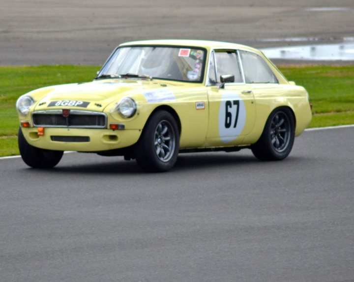 MGC vs V8 - Which is the best GT ? - Page 1 - MG - PistonHeads - The image shows a vintage racing car on a track. The car is painted in a bright yellow color with white racing stripes. It bears the number "67" prominently displayed on the hood and side. The car is equipped with a roll cage and a strut brace, indicating that it is prepared for hard racing conditions. The vehicle has black wheels and the track appears to be wide and well-maintained.