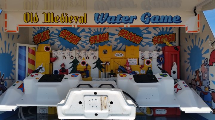 A bathroom with a toilet and a sink - Pistonheads - The image showcases a vibrant, old-fashioned arcade game. The central theme of the game is medieval, featuring a life-size caricature of King Arthur with his castle in the background. The color palette of the game includes shades of yellow, blue, and red, contributing to its lively and whimsical atmosphere. The game is designed with multiple seating areas, accommodating numerous players at once, and is likely a shooting or target game, as indicated by the targets set up in the scene. The red buttons in the foreground and the text "Old Medieval Water Game" suggest interactive controls and a water-based gameplay. The overall setting seems to be indoors, possibly in an arcade or entertainment venue.