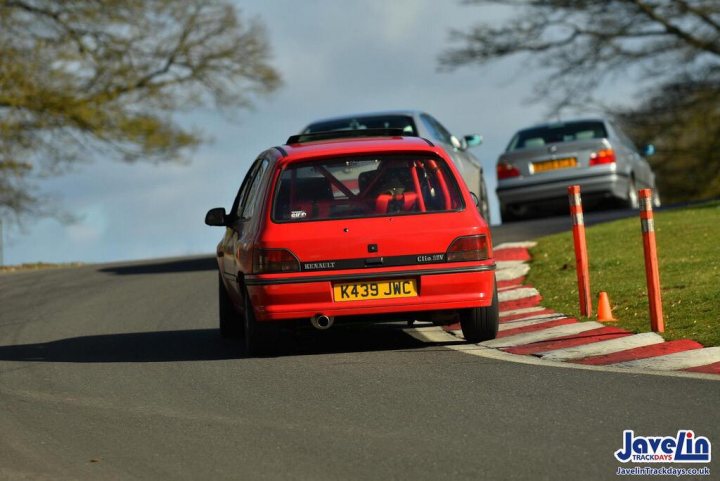 A Caravan of Clios - Mk1 16v, Mk2 Sports - Page 2 - Readers' Cars - PistonHeads - The image depicts a dynamic scene on a winding mountain road. A red car is in motion, captured mid-turn on the asphalt road. Other vehicles are also present, adding to the sense of movement. Barriers line both sides of the road, suggesting it's a controlled environment for drivers. In the background, a clear sky and lush greenery paint a serene and picturesque setting.