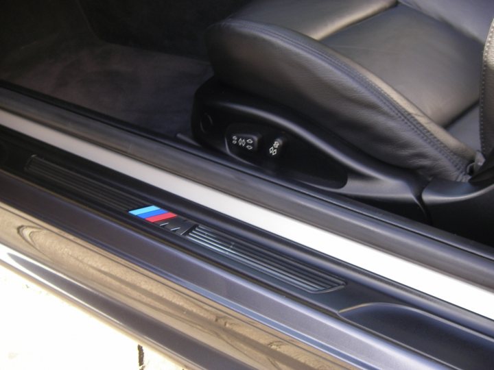 Pistonheads - The image displays the interior of a car door, viewed from the side. The door has a dark blue panel with a central white stripe, possibly demarcating areas for handles or switches. There is a red, white, and blue label near the bottom right corner of the panel, which might be a dealership sticker or a manufacturer's emblem. The car's dashboard is barely visible at the bottom edge of the image, and the door latch is located near the top of the panel, adjacent to the dashboard.