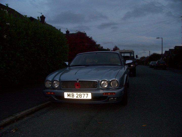 Show us your Daily driver, and Weekend Toy(s)!!! - Page 3 - Readers' Cars - PistonHeads - The image shows a single silver car parked on a dark, asphalt road. The car, which has a red flower on the front, is the main subject of the photo. In the background, there are other cars parked and a street sign visible. This quiet street scene suggests it might be late afternoon or early evening due to the subdued lighting.