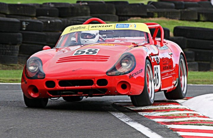 All my racing in 2014 should - Page 1 - Dunlop Tuscan Challenge - PistonHeads - The image depicts an intense scene on a racetrack. A bright red race car, numbered 58, is prominently featured in the foreground, driving along the track. It bears the number 98 and the Herson brand logo. The car is seen tire-to-tire with a tire barrier on the left, indicating that this could be a challenging section of the track. The driver seems focused and is likely a professional racer participating in a competitive race. The track is bordered by green grass, suggesting that it is a permanent circuit rather than a temporary setup.