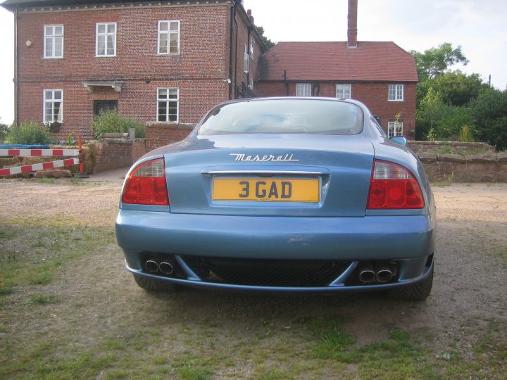 Show us your REAR END! - Page 221 - Readers' Cars - PistonHeads - This image shows a dark blue Peugeot 306 car parked on a gravel driveway in front of a large brick house. The license plate on the car reads "3GAD". The car features red taillights and has a sporty appearance with a hood scoop. The house behind the car has a tiled roof and there are other vehicles and buildings in the background, suggesting a suburban setting.