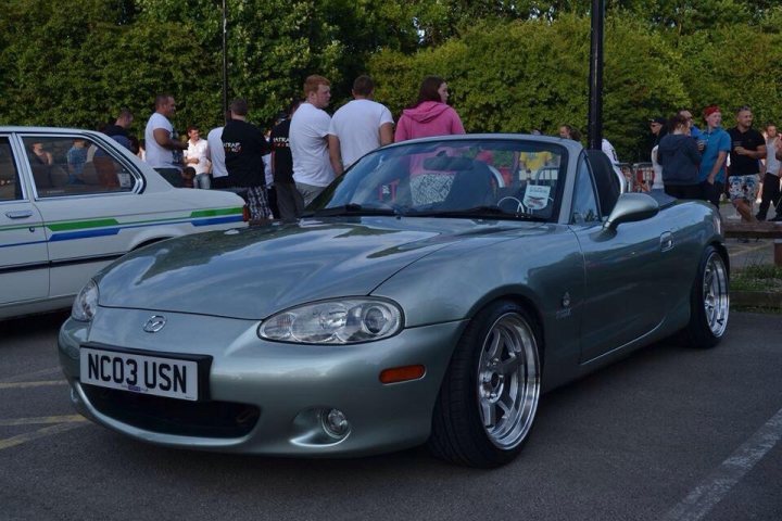 A car is parked in a parking lot - Pistonheads - The image captures a vibrant scene at a car show. The main focus is on a silver car, a Mazda Miata, parked in the center of the image. The Miata sports a black vinyl wrap and tinted windows, giving it a sporty and sleek look. 

Surrounding the Miata is a crowd of people, some of whom are gathered around the car, possibly admiring the modifications or discussing the car's details. The setting appears to be a parking lot adjacent to a grassy area, creating a pleasant contrast between the urban and natural elements. 

The image beautifully encapsulates the spirit of a car show, where enthusiasts come together to celebrate their passion for cars.