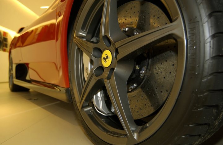 LaFerrari - is this an 'extra' Ferrari option? - Page 1 - Ferrari V12 - PistonHeads - The image features a close-up view of an exotic sports car, focusing on its front wheel. The tire is half encased with a boundary line, indicating it's in a designated area, likely a showroom or auto garage. The car's wheel wells, painted a vibrant shade of orange, stand out against the rest of the car, highlighting its unique design. On the metal hubcap inside the wheel well, there's a small yellow logo, distinctively marked as a Ferrari emblem, symbolizing the luxury and high-performance nature of the vehicle. The contrast between the shiny silver hubcap and the black tire reveals a well-maintained automobile, with meticulous detailing visible on the vehicle's exterior.