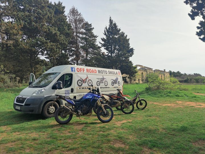 Every day tips for living with a 599 - Page 39 - Ferrari V12 - PistonHeads UK - The image shows a grassy field where two motorcycles are parked. To the left, there is a blue and white motorcycle with its kickstand down, partially obscured by a van that is parked nearby. On the right side of the image, another motorcycle is visible, standing on its kickstand. A dirt road or trail is discernible in the background, indicating that this could be a rural area or perhaps near some outdoor recreation areas. The sky appears overcast, suggesting it might be a cool day or it's possibly late afternoon. There are no people present in the image, and the focus seems to be on the vehicles themselves and their arrangement in the field.