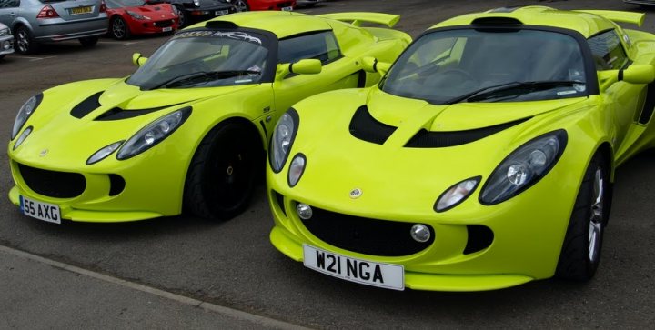 A brace of Exige - Page 1 - Elise/Exige/Europa/340R - PistonHeads - The image presents a striking scene of several green sports cars parked closely together. The cars, with their vibrant green color and sleek designs, are the main focus of the image. They are aligned in parallel, creating an almost rhythmic pattern. The setting seems to be a winding road or a small lot, as the cars are surrounded by a variety of other vehicles. The overall atmosphere of the image is dynamic and exciting, matching the sporty nature of the cars themselves.