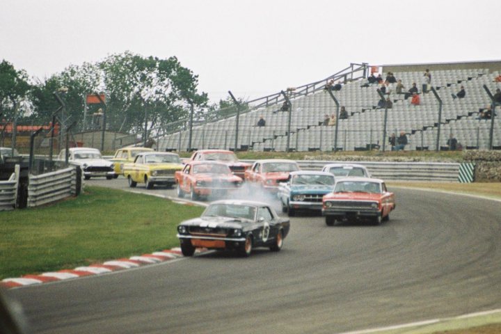 Historic Hatch Brands Pistonheads - The image captures a dynamic scene at a car race on a track. Several cars, in various positions, are speeding along the track. The cars range from smaller, more aerodynamic models to larger, more robust ones. The vehicles are partially obscured by the intense racing action and the motion blur suggests high speed. In the background, there are spectators seated in stands, adding to the excitement and intensity of the race.