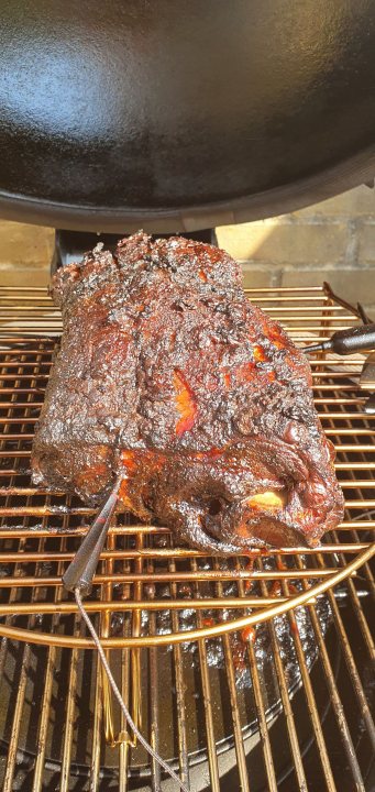 The bbq photo & recipe thread - Page 158 - Food, Drink & Restaurants - PistonHeads - The image shows a large, cooked piece of meat on a grill. It has a rich brown color and appears to be smothered in sauce or glaze. In the background, there's an outdoor cooking setup with a BBQ grill and what looks like a gas tank, suggesting that this might be a backyard barbecue setting. The photo is taken from a distance, so the focus is primarily on the food, not the surroundings. There are no people visible in the image.