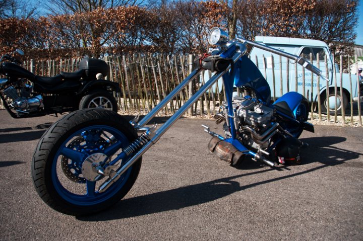 Pistonheads - The image showcases a dark-colored motorcycle parked on a concrete surface. It stands out with its blue wheel and chrome details, giving it a custom look. In the background, there's another motorcycle and a blue truck, indicating that this might be at a gathering or event focused on vehicles. The overall scene suggests a day of leisure, possibly a motorcycle meet-up or an outdoor event where these vehicles are admired.