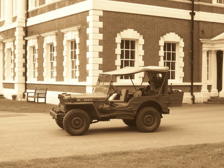 my new Jeep - Page 1 - Off Road - PistonHeads - The image portrays a scene from a previous era, featuring an old Model B Jeep parked on a street. The jeep exhibits a faded olive green color, hinting at its vintage nature. Two people are seated in the open-top jeep, suggesting an effortless sightseeing experience. The buildings in the background with their round window arches and white panels give the scene a quaint, old-town appeal. Despite the sepia tones, one can feel the sense of adventure and exploration associated with such journeys.