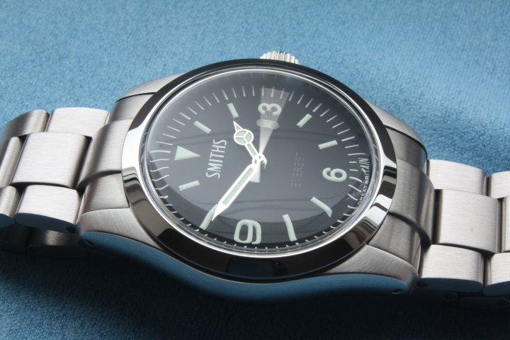 A close up of a clock on a wall - Pistonheads - A close-up view of a silver watch with a black face and white digital markings. The watch is adorned with three smaller dials, including a date window. It is placed on a blue fabric background, with the watchstraps slightly visible. The silver buckle and clasp, typical of luxury watches, add to the overall elegance of the timepiece.