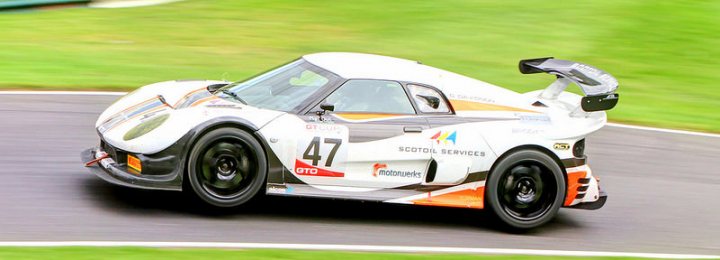 A white and black motorcycle is parked in a parking lot - Pistonheads - The image shows a white race car with the number 47 on its silver and orange livery, in motion on a curved race track. The car has a massive rear wing that is extended to adjust to air pressure. The tireview is not in their home country but rather in the United Kingdom as evidenced by the UK license plate. The background is a blur of green and white, emphasizing the speed of the vehicle.