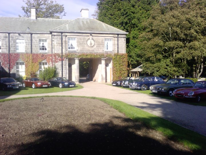 Newcastle Hotel Pistonheads - The image features a large, two-story building that appears to be an important structure, possibly a historic estate. In the front of the building is a sizable entryway, round with full-height pillars flanking the pathway leading to a set of towering doors at the center. The building appears to be constructed of stone, giving it a stately and grand appearance.

Directly in front of the building, there is a spacious parking lot filled with a variety of luxury cars. The cars are arranged in a cluster, with several different brands and models visible. The setting suggests an event or gathering at the building, likely related to the vehicle owners' interest in classic or luxury cars.