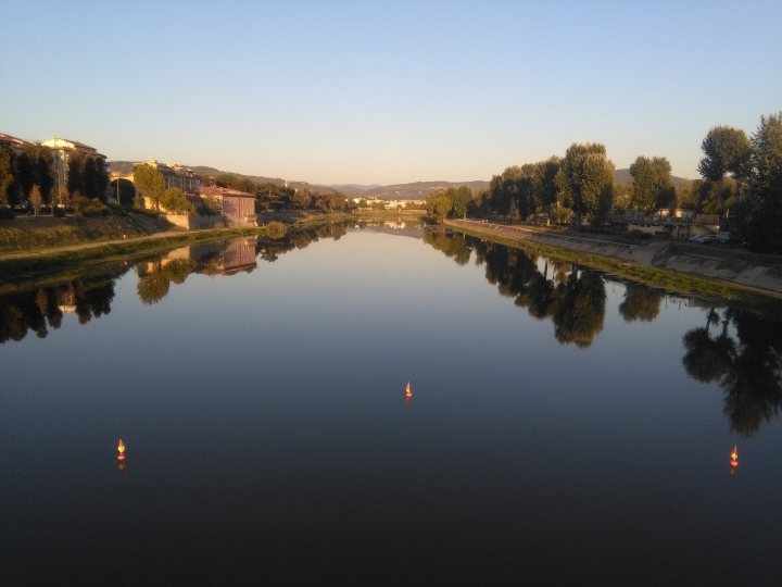 A view of a river with a bridge in the background - Pistonheads - The image captures a serene scene of a river flowing through the center of an urban area. The river, reflecting the sky and the surrounding buildings, stretches out towards the horizon where trees can be seen. On either side of the river, there are trees and buildings that line the banks. A boat is visible on the waterway, adding to the peaceful ambiance of the scene. The reflection of the cityscape in the river water enhances the beauty of the image.