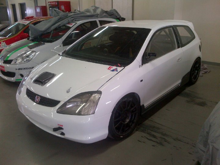 Any of you lot know this Race Car - Page 1 - Middle East - PistonHeads - This image shows a white Honda Civic hatchback car parked inside a workshop or garage area. The car is adorned with a motorsport foreground sticker, indicating its association with sports car events or team. The vehicle appears to be well-maintained and polished, reflecting the light off its various surfaces. In the background, another car is partially visible, suggesting that this space is used for parking multiple vehicles. The floor is marked with tire marks, indicating that other vehicles had been moved recently. The overall atmosphere of the image is one of care and attention, emphasizing the significance of the white Honda Civic as the main subject within the scene.