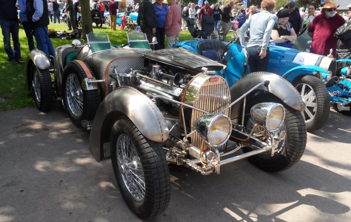 Prescott Vie en bleu this weekend! - Page 1 - South West - PistonHeads - The image showcases a collection of vintage cars parked on a road or parking area. Crowds of people can be seen walking around and admiring the vehicles. One car, a Model T replica, stands out prominently in the scene, highlighting its antique design. The setting suggests a car show or exhibition where enthusiasts gather to appreciate these classic automobiles.