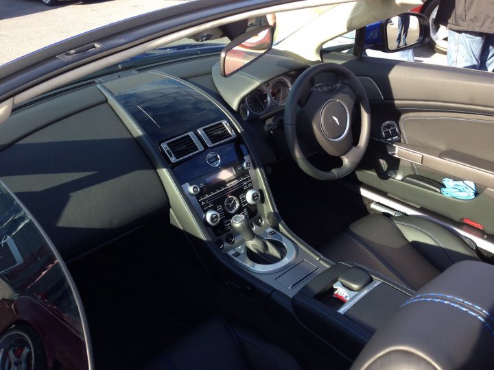 South West Wales Breakfast Meet - Page 143 - South Wales - PistonHeads - The image captures the interior of a convertible car, viewed from the passenger side. The black leather driver's seat is positioned on the left, revealing the centralized console of the vehicle. The dashboard is neatly arranged, although the dust on the air vents is visible. The sun is shining on the car, creating bright spots and enhancing the details of the car's interior, such as the steering wheel, which features the Nissan emblem in the center. Beyond the car, one can see aspects of the road and the setting sunlight, suggesting the image was taken either during sunrise or sunset.