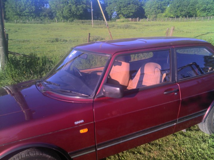 An old car is parked in the grass - Pistonheads - The image depicts a red, four-door hatchback parked in a grassy area, likely a field or a lawn. The car has a distinct shape, characteristic of older hatchbacks, with a sloping front windshield and a pronounced hatchback at the rear. There is a visible label on the car's rear side door that reads "SAPPHIRE," but it's not clear if it's part of the vehicle's branding or a separate decal. The setting suggests a rural or semi-rural environment, as there's an open sky and what appears to be a wooden fence or dividing line in the background. The grassy area appears well-maintained, indicating that it might be a domestic property such as a driveway or a garden area associated with a house.