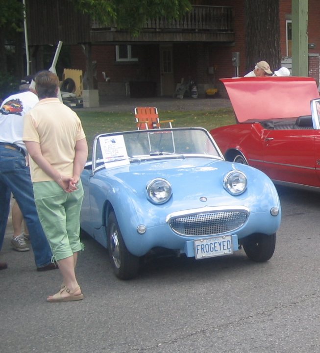 Storage Summer Years Pistonheads - The image features an outdoor setting where a vintage blue car and a red convertible are parked on the street. A man is examining the blue car, which stands out due to its old-fashioned design, bright color, and prominent grille. The car is parked near a sidewalk where people are walking by. There is also an orange chair positioned near the car, perhaps suggesting an outdoor event or gathering. The scene is casual and lively, evoking a sense of a pleasant day spent outdoors.