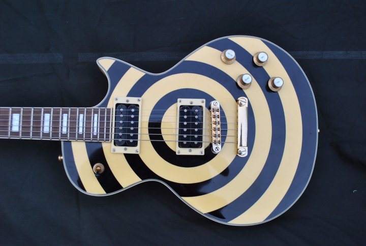 Fake Epiphone Les Paul Zakk Wylde on eBay?  - Page 1 - Music - PistonHeads - The image showcases a portion of a striking electric guitar with a striking blue and yellow graphic on it. The guitar's body is painted in alternating blue and yellow stripes, producing an eye-catching contrast against the black background. The pickups are golden in color, adding a touch of elegance. The guitar string displayed in the image comprises six parallel strings, indicating it's a six-string electric guitar. The year the guitar was made, 1988, is visible in the image, suggesting its age and history.