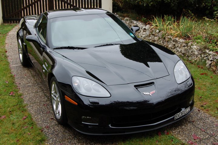 Pistonheads - In the image, a prestigious sports car, possibly a Corvette, is parked on a driveway. Its black exterior gleams in the sunlight, contrasting with the gray gravel of the driveway. The car is positioned facing towards the left side of the image. The landscape in the background is dominated by verdant shrubs and trees, providing a serene backdrop to the sleek vehicle. The overall scene suggests a tranquil suburban setting, with the sports car hinting at a sense of luxury and speed.